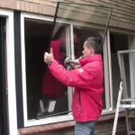 Vitrier professionnel retirant un vieux simple vitrage pour installer un double vitrage HR++ sur un châssis en bois conservé à Anderlecht.